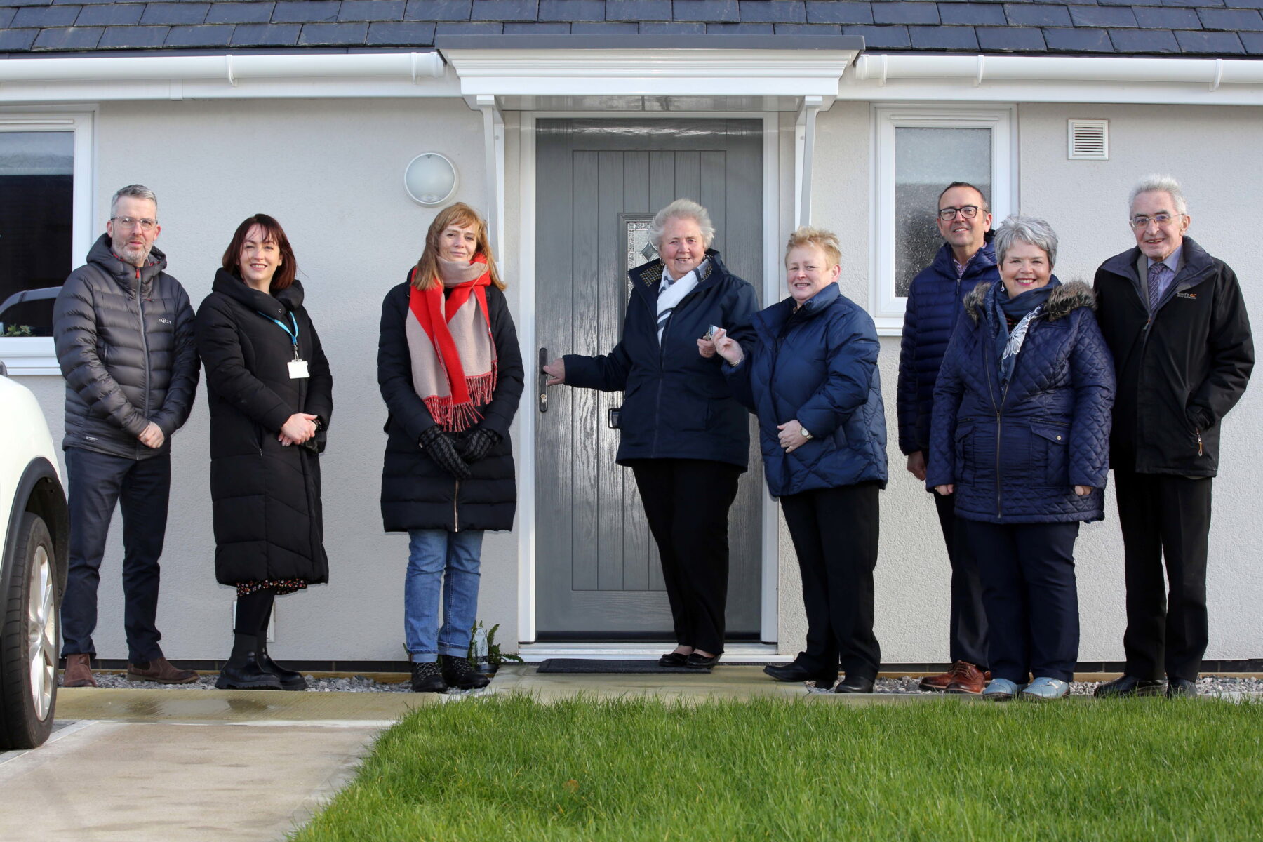 Mrs Eleanor Williams outside her new Grwp Cynefin home in Llain Delyn, Gwalchmai ,with L-R: Grwp Cynefin Director ,Mel Evans;,GC Housing Officer, Llinos Jukes; GC Board Member, Llinos Iorweth; GC Chief Executive ,Shan Lloyd Williams ; Ned Michael, Head of Anglesey Housing ; Carys Edwards GC Chair and Anglesey Councillor, Alan Mummery